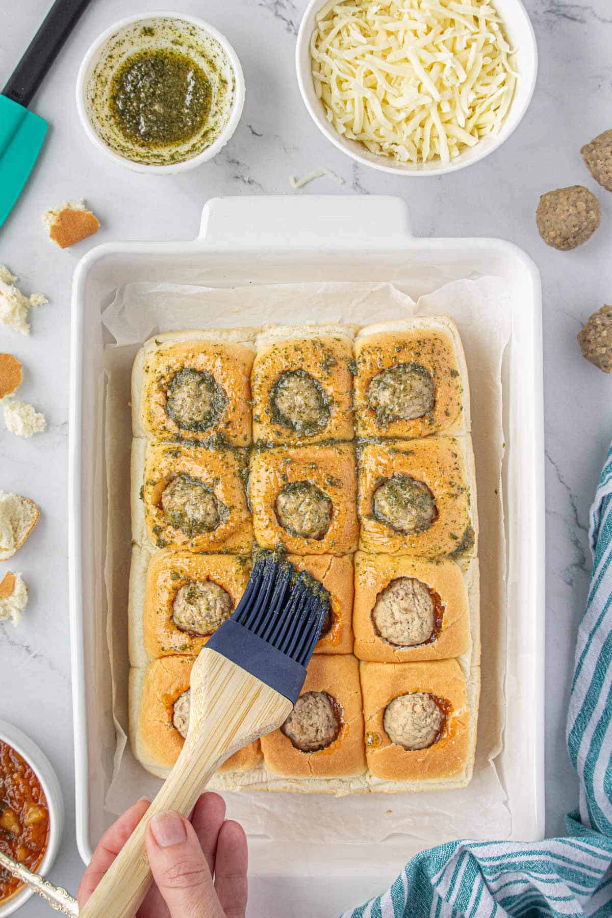 Meatball sliders being brushed with seasoned butter before baking.