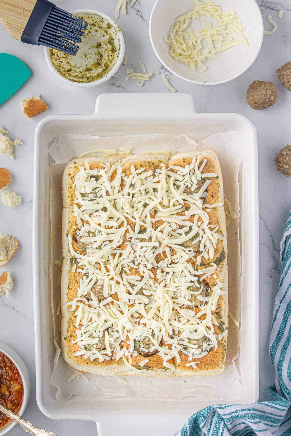 Meatballs sliders topped with mozzerella cheese and ready to put into the oven to be baked.