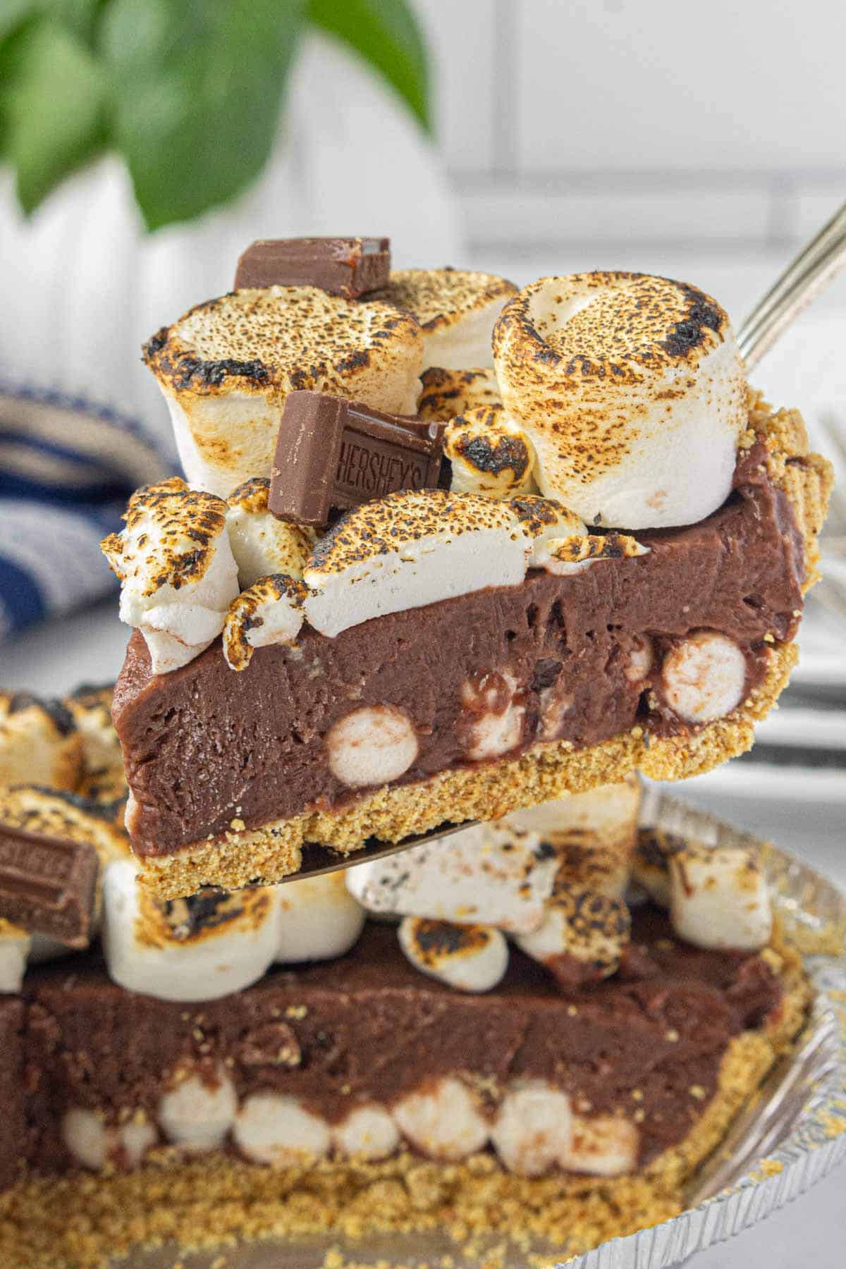 A slice of no-bake s'mores pie just sliced from the pie and held up by a cooking spatula.