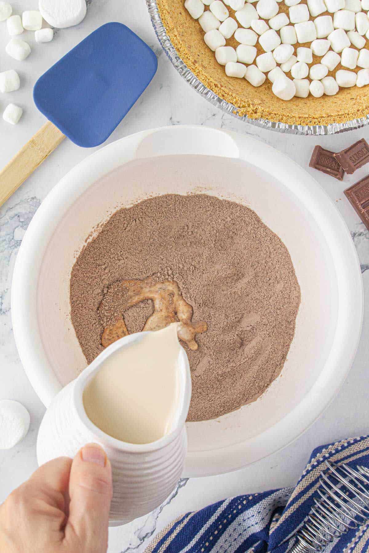 Chocolate pudding mix in a large mixing bowl. Milk is being poured into the mix.