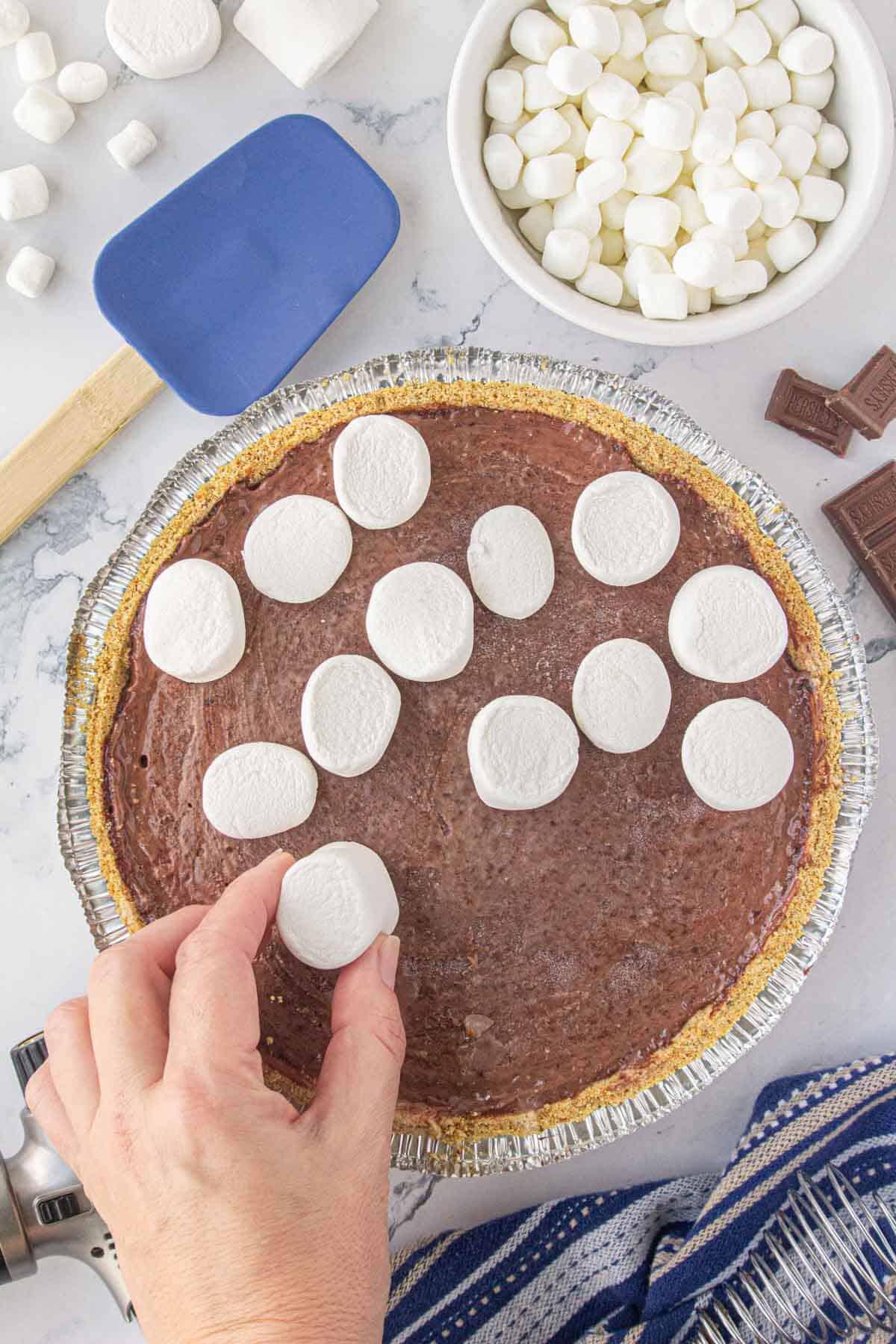 Chocolate pudding pie in a graham cracker crust being topped with marshmallows.