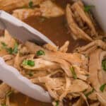 Slow cooker honey garlic chicken in a crockpot with tongs for serving the shredded chicken.