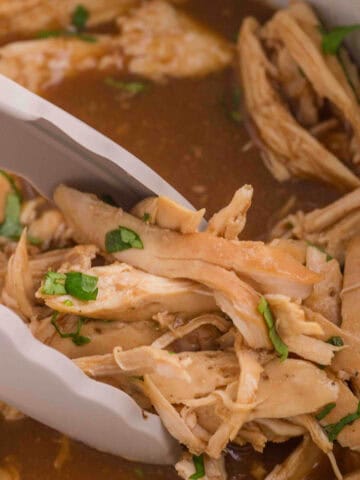 Slow cooker honey garlic chicken in a crockpot with tongs for serving the shredded chicken.