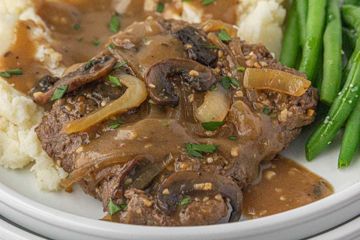 Cube steak on a plate smothered in an onion, mushroom gravy. Served with mashed potatoes and green beans.