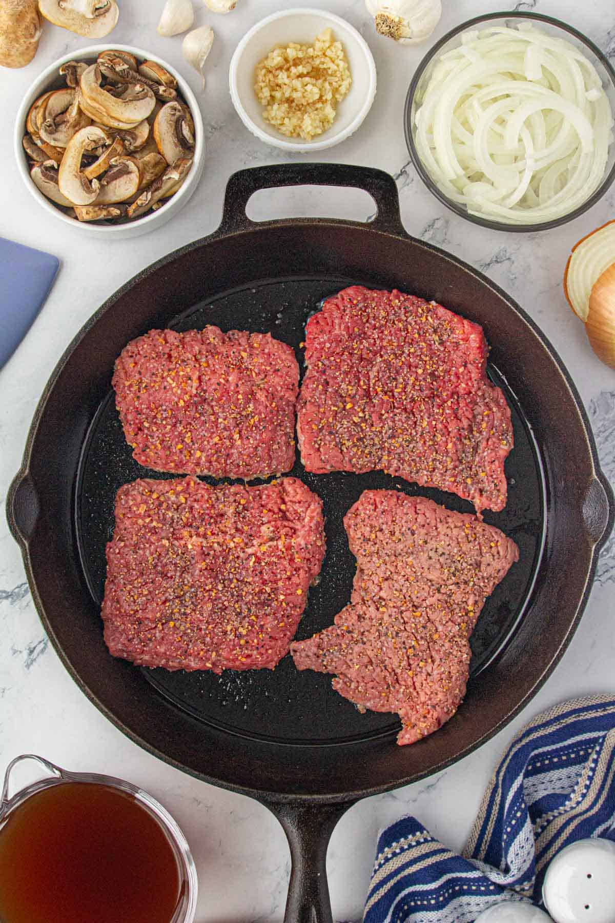 Cube steak being sauteed in a cast iron skillet.