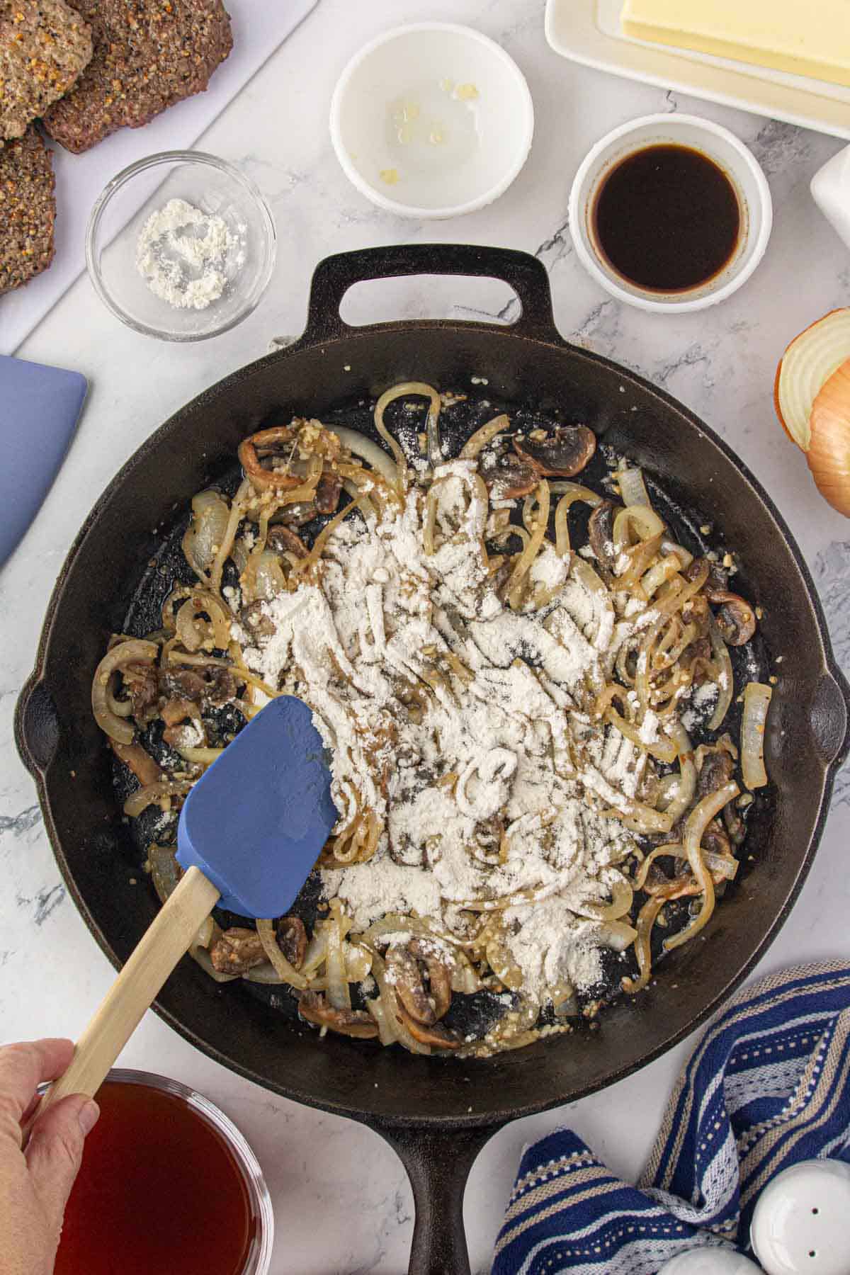 Flour sprinkled over sauteed mushrooms and onions in a cast iron skillet.