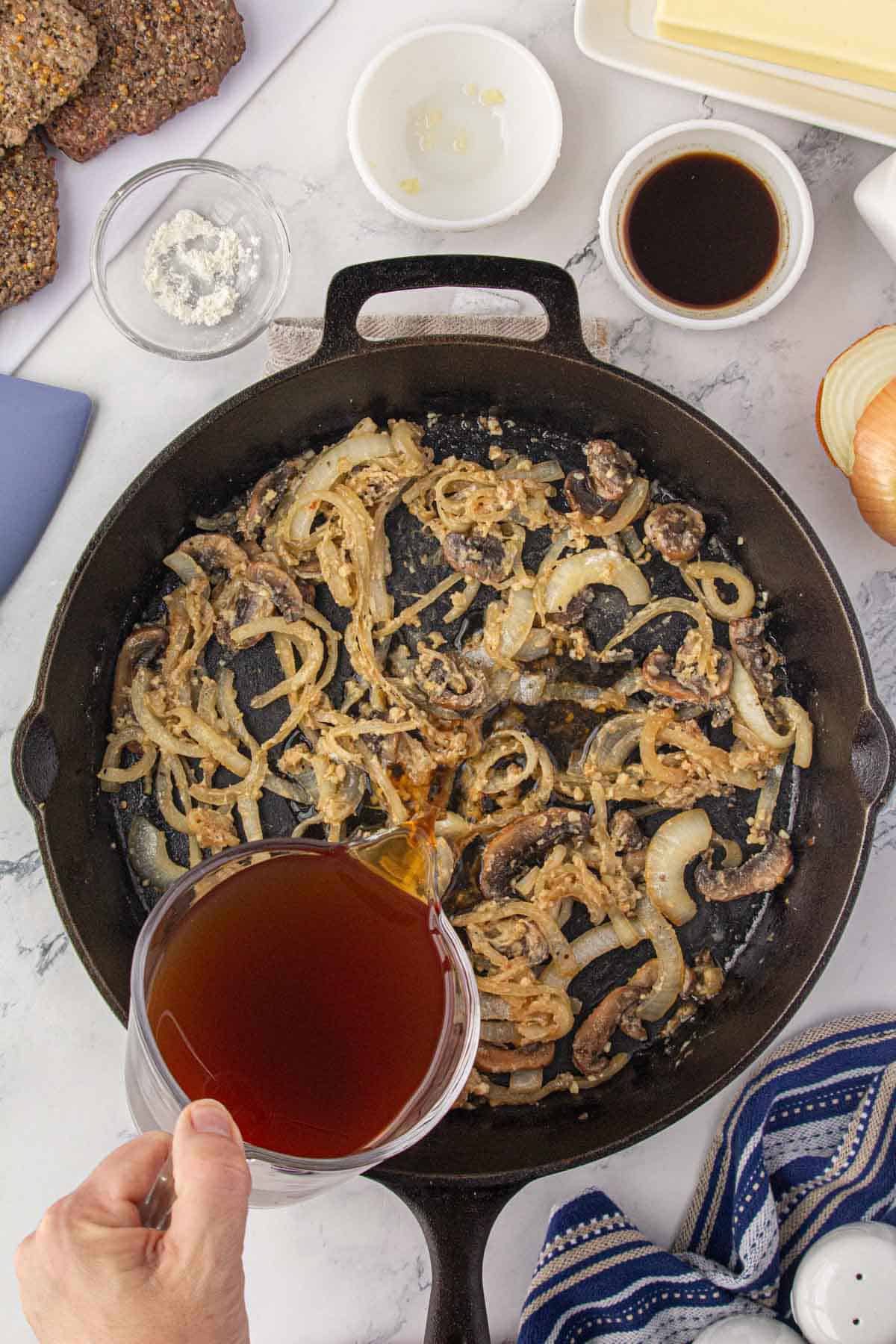 Sauteed mushrooms, onions and garlic in a skillet. Flour was sauteed with the vegetables and now beef stock is being poured into the skillet to make gravy.