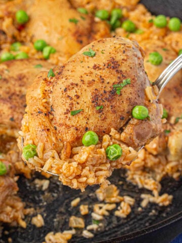 Seasoned cooked chicken thighs with rice in a skillet.