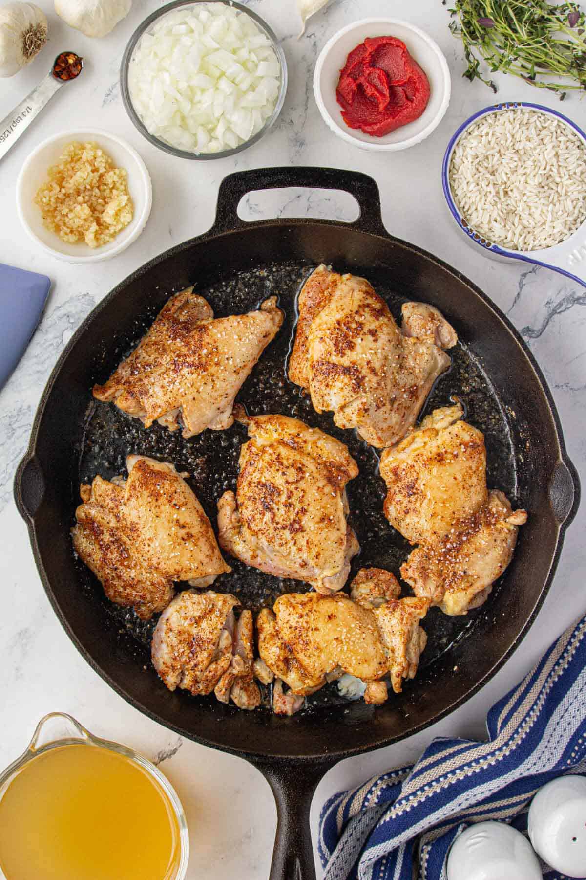 Seasoned chicken thighs frying in a skillet.