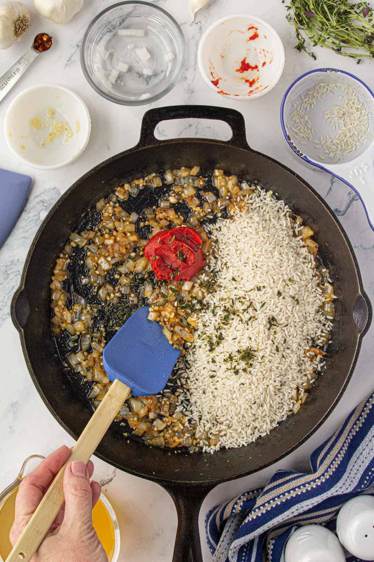 Aromatics sauteing in a pan. Long grain rice has been added and it's being stirred into the onion garlic mixture.