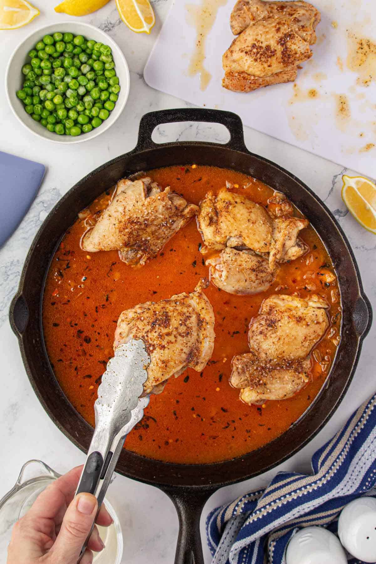 Seared chicken thighs are being nestled into the saucy rice mixture in a skillet.