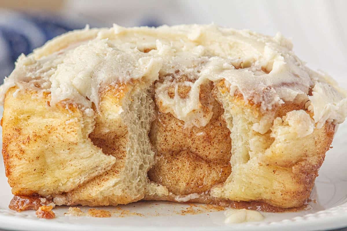 A cinnamon roll on a plate that has a bite taken out of it.