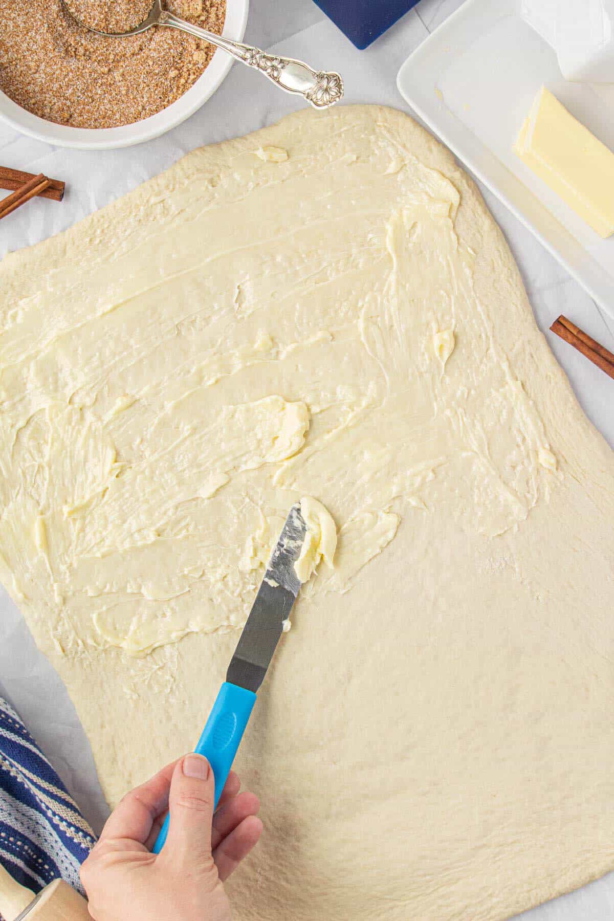 Butter being spread on dough for cinnamon rolls.