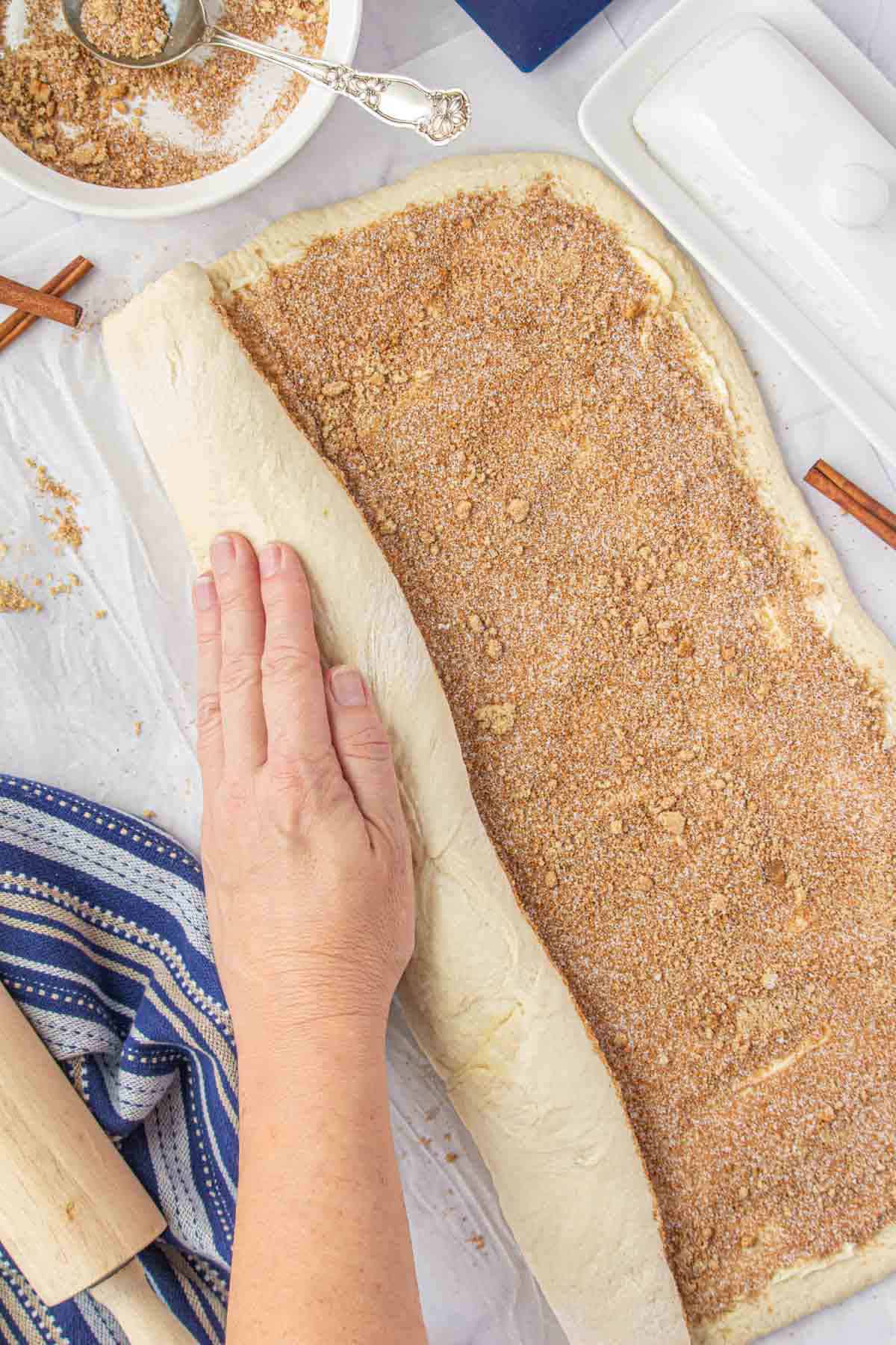 Cinnamon rolls dough being tightly rolled into a log prior to slicing.