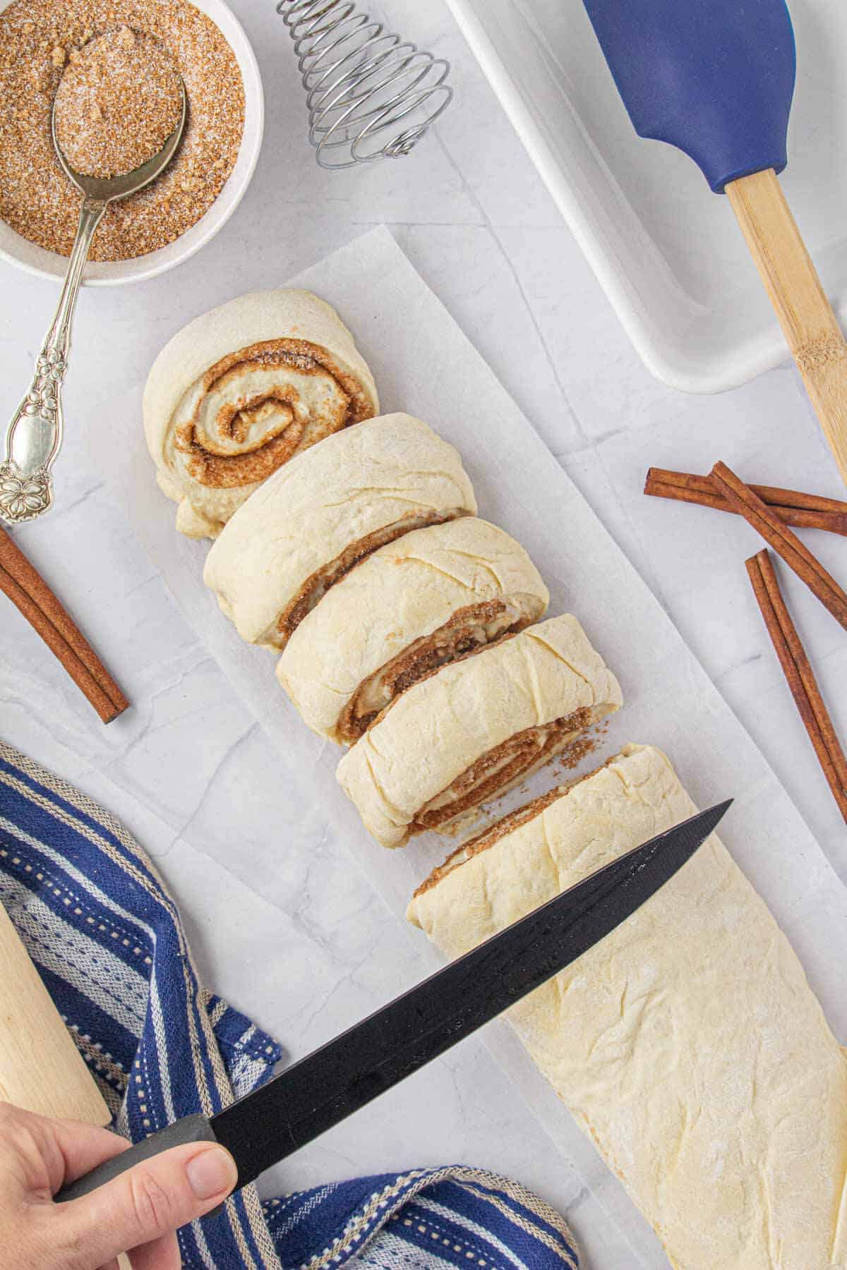 Cinnamon rolls dough being sliced with a knife.