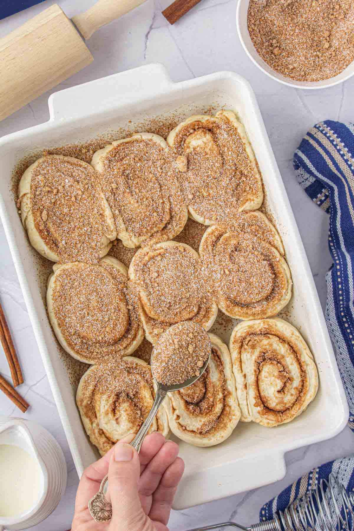 Cinnamon rolls in a baking dish. Cinnamon sugar mixture being sprinkled on the rolls prior to baking.