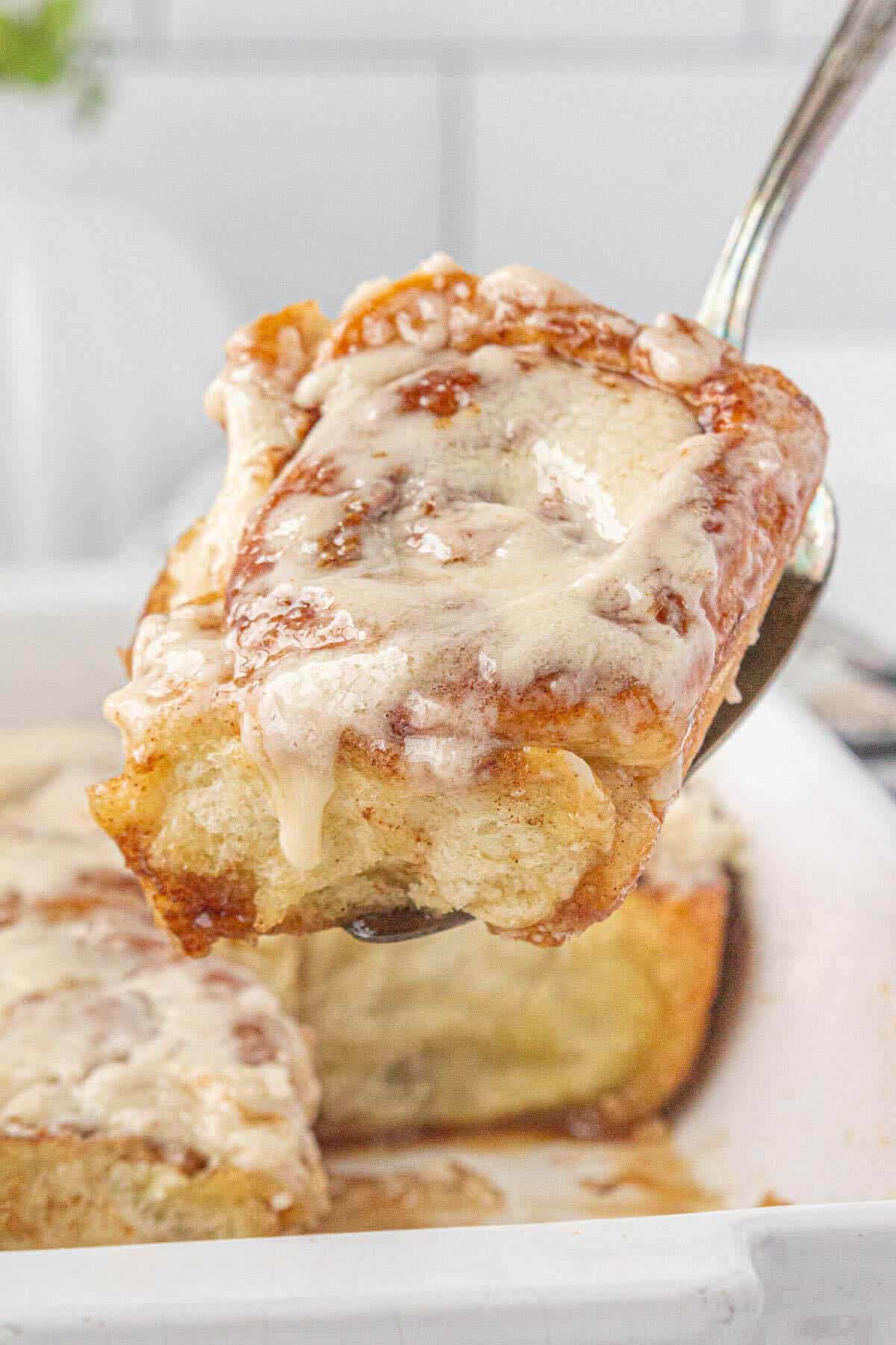 A warm cinnamon roll removed from the baking dish. It's hot and the icing is drizzling over the side of the roll.