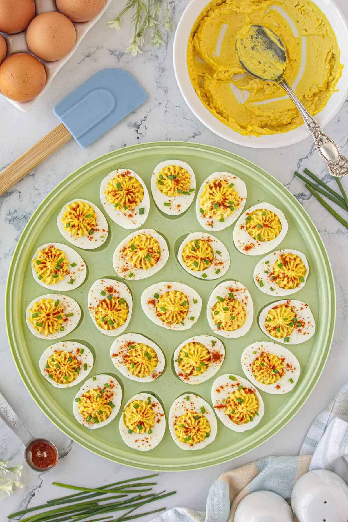 Deviled eggs on an egg platter decorated with sliced chives and paprika.