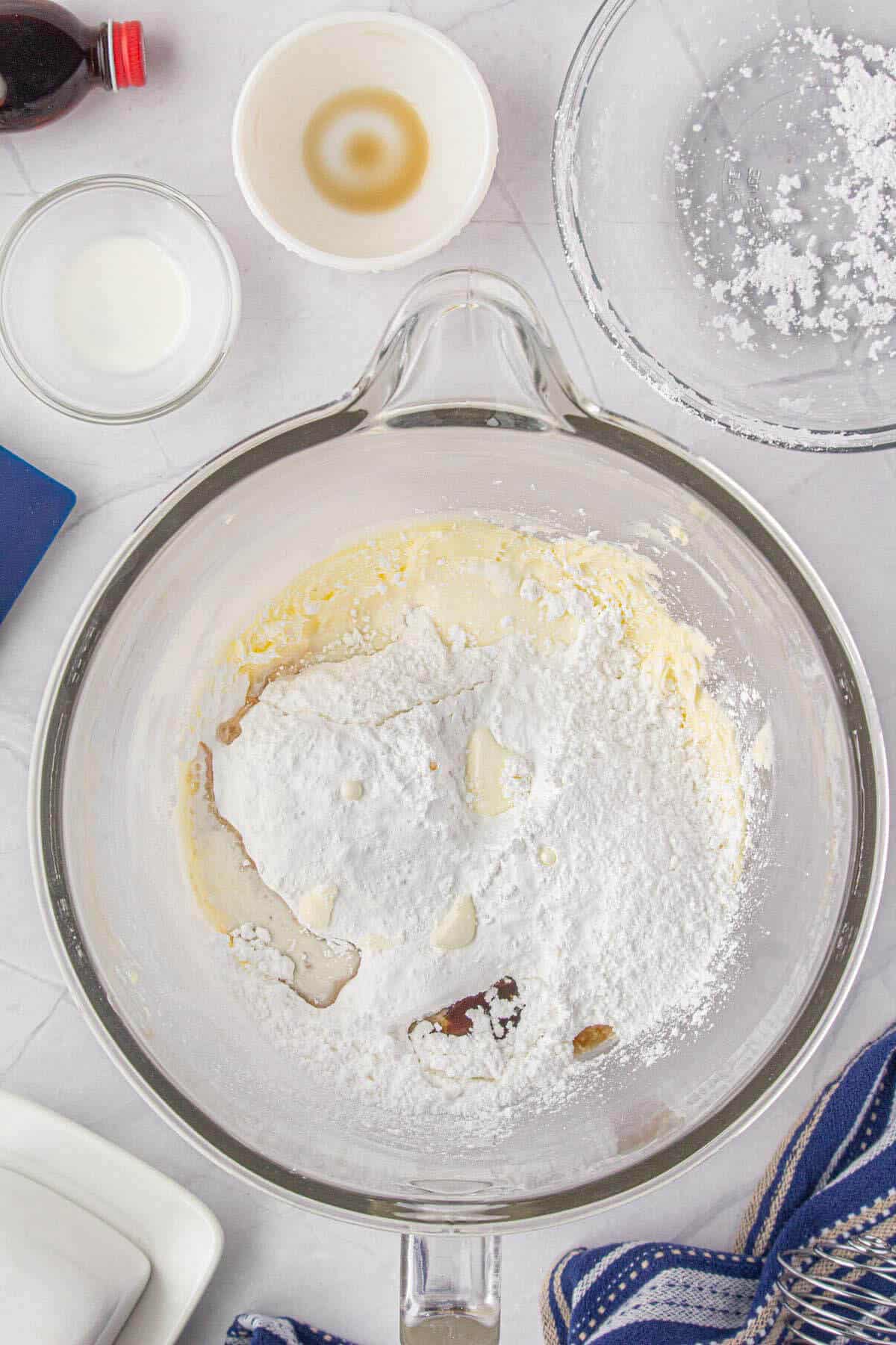 Powered sugar added to creamed sugar in a mixing bowl.