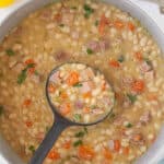 A big soup pot filled with ham and bean soup, with a ladle scooping up a serving.