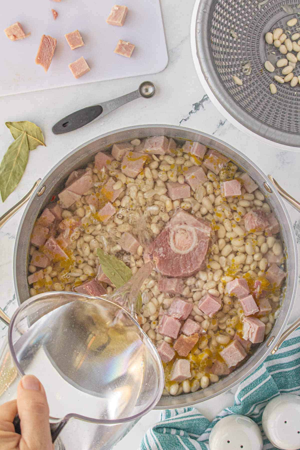 Dried beans and ham in a soup pot, with water poured into the pot.