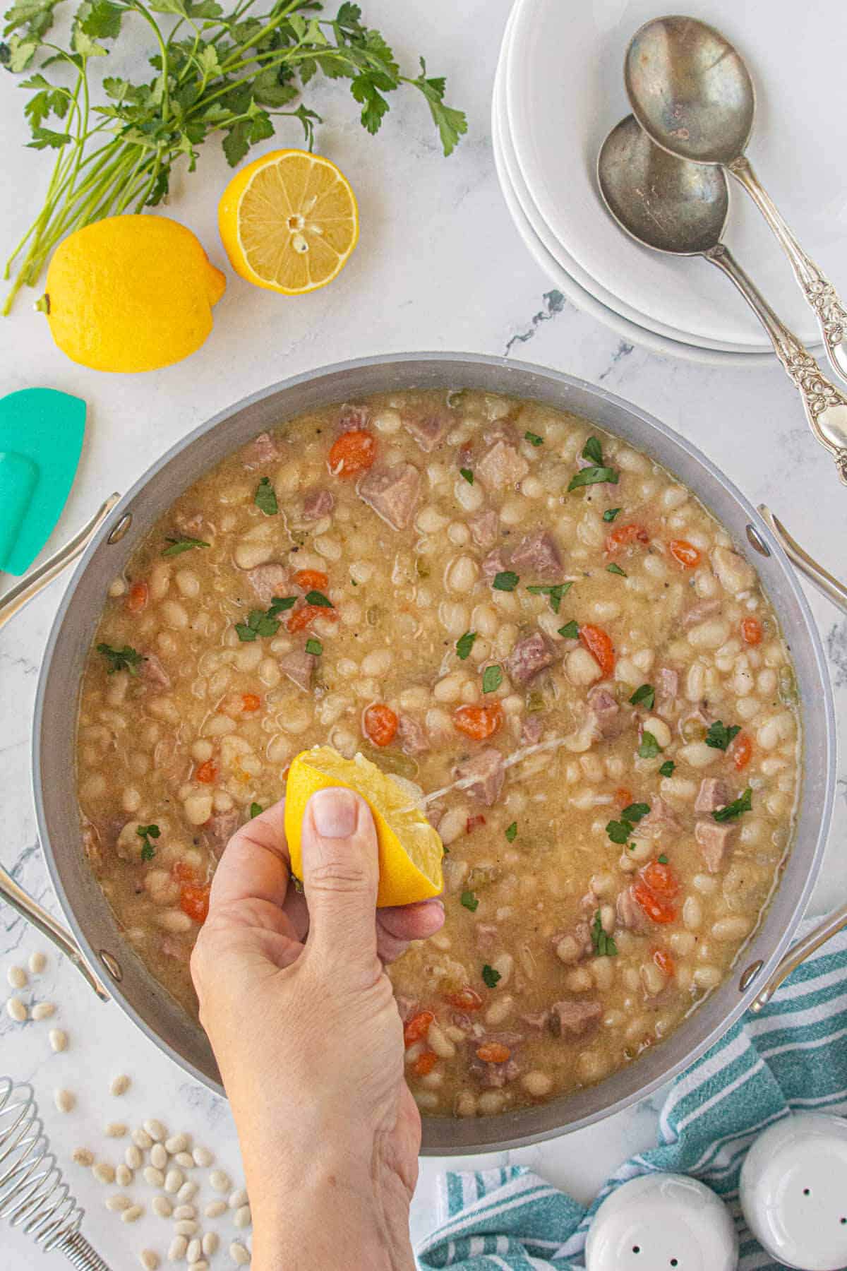 A finished pot of navy bean soup with a hand squeezing lemon into the soup pot.