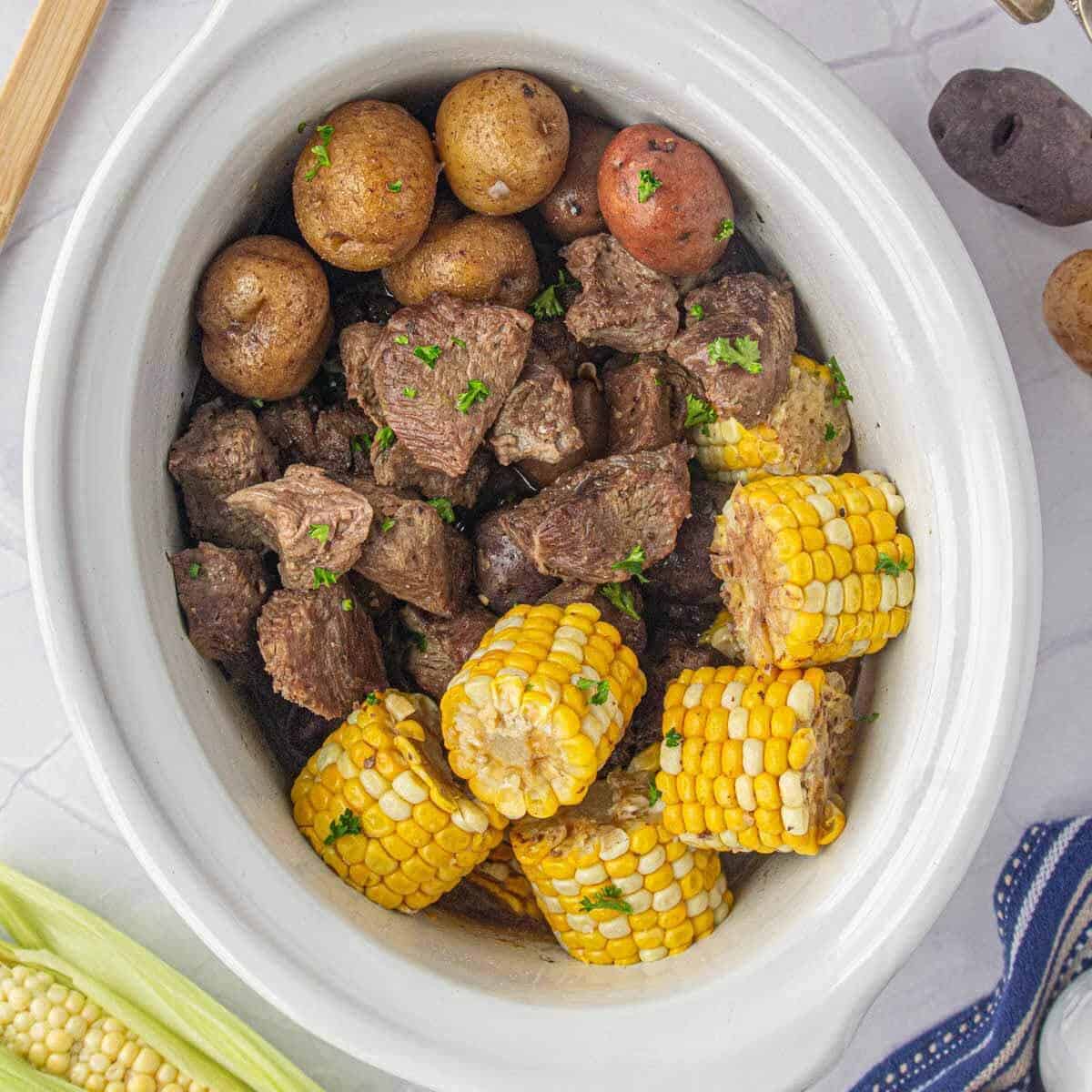 Cooked garlic butter steak bites, potatoes and corn in a slow cooker.
