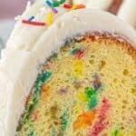 A slice of colorful confetti Bundt cake topped with thick cream cheese frosting and rainbow sprinkles, with text overlay reading "Copycat Confetti Cake – Family Favorite!".