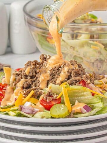 A close-up of Big Mac Salad on a plate, featuring layers of lettuce, ground beef, pickles, onions, and sesame seeds, drizzled with creamy dressing.