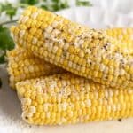 Plated slow cooker corn on the cob sprinkled with black pepper and parmesan cheese.