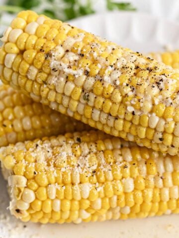 Plated slow cooker corn on the cob sprinkled with black pepper and parmesan cheese.