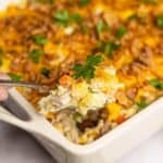 Spoonful of creamy chicken casserole topped with cheddar cheese, vegetables, and crispy onions, garnished with fresh parsley.
