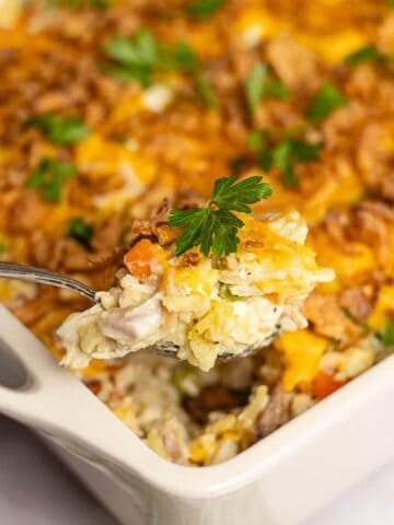 Spoonful of creamy chicken casserole topped with cheddar cheese, vegetables, and crispy onions, garnished with fresh parsley.