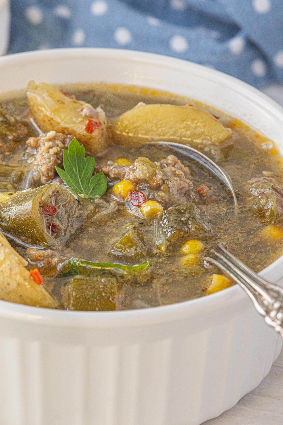 White bowl of sausage and okra stew with potatoes, corn, and herbs in a savory broth.