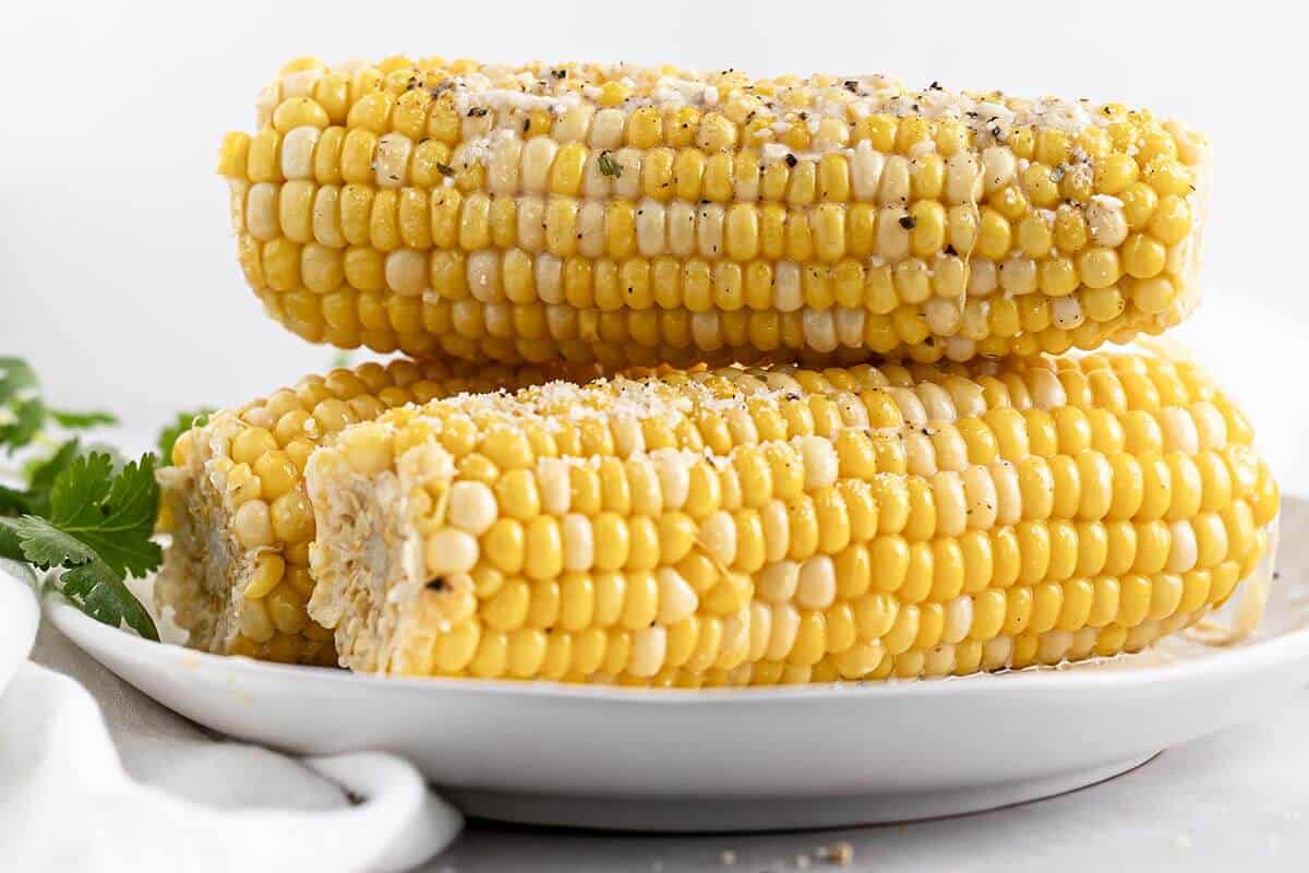Cooked corn on the cob plated and topped with pepper and grated cheese.