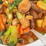Closeup of saucy Crockpot chicken stir fry with chunks of chicken, broccoli, carrots, mushrooms, and sesame seeds.