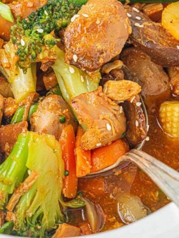 Closeup of saucy Crockpot chicken stir fry with chunks of chicken, broccoli, carrots, mushrooms, and sesame seeds.