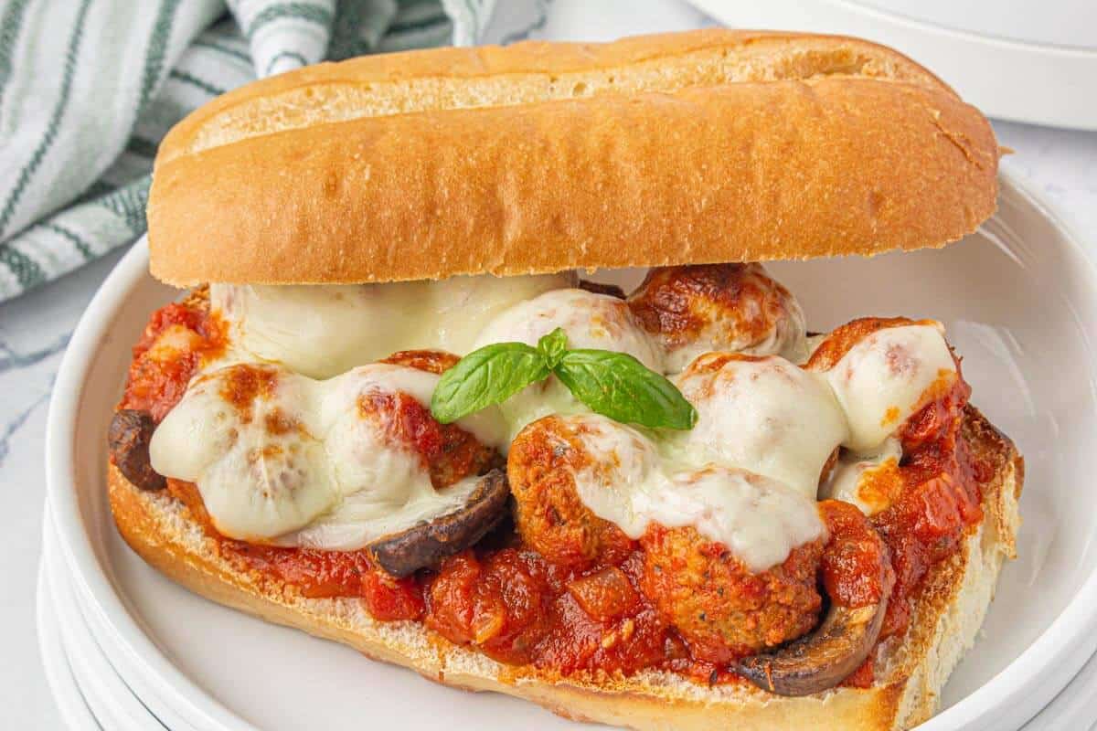 Toasted hoagie roll stuffed with marinara meatballs, mushrooms, and melted mozzarella cheese, garnished with fresh basil.