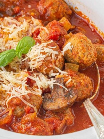 Close-up of a slow cooker filled with marinara meatballs, garnished with grated parmesan and fresh basil.