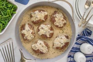 Skillet full of seared ground beef patties simmered in cream of mushroom gravy, ready to serve.