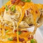 Cheesy spoonful of bubble up chicken casserole being lifted from a baking dish, with melted cheddar, bacon, and green onions. Text overlay reads “Bubble Up Chicken Casserole – Great for Potlucks.”