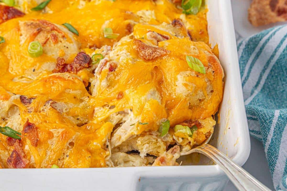 Close-up of the golden biscuits and melty cheese bubbling on top of the bubble-up chicken casserole, with a serving spoon.