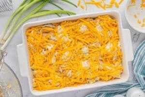 The casserole mixture fully combined with biscuit dough pieces in baking dish topped with shredded cheese.
