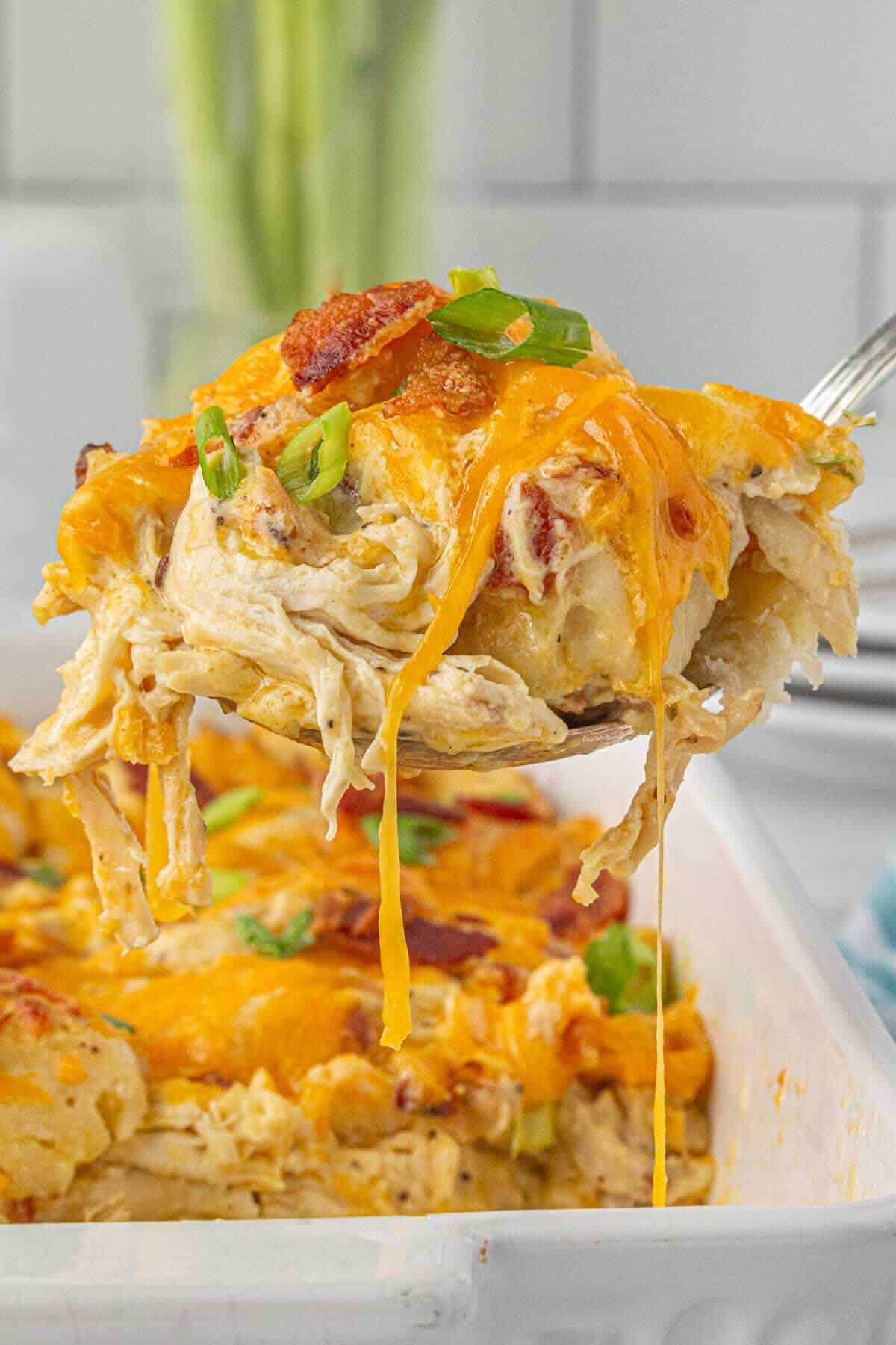 A cheesy spoonful lifted from the pan showing the creamy, gooey texture and bits of bacon and green onion.