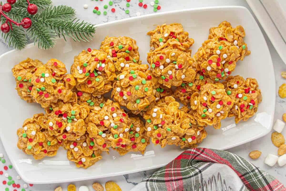 Overhead view of a rectangular white serving tray filled with peanut butter cornflake cookies, decorated with holiday sprinkles and surrounded by Christmas greenery.