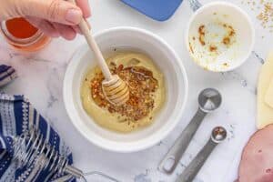 Mustard, honey and spices being combined in a small mixing bowl.
