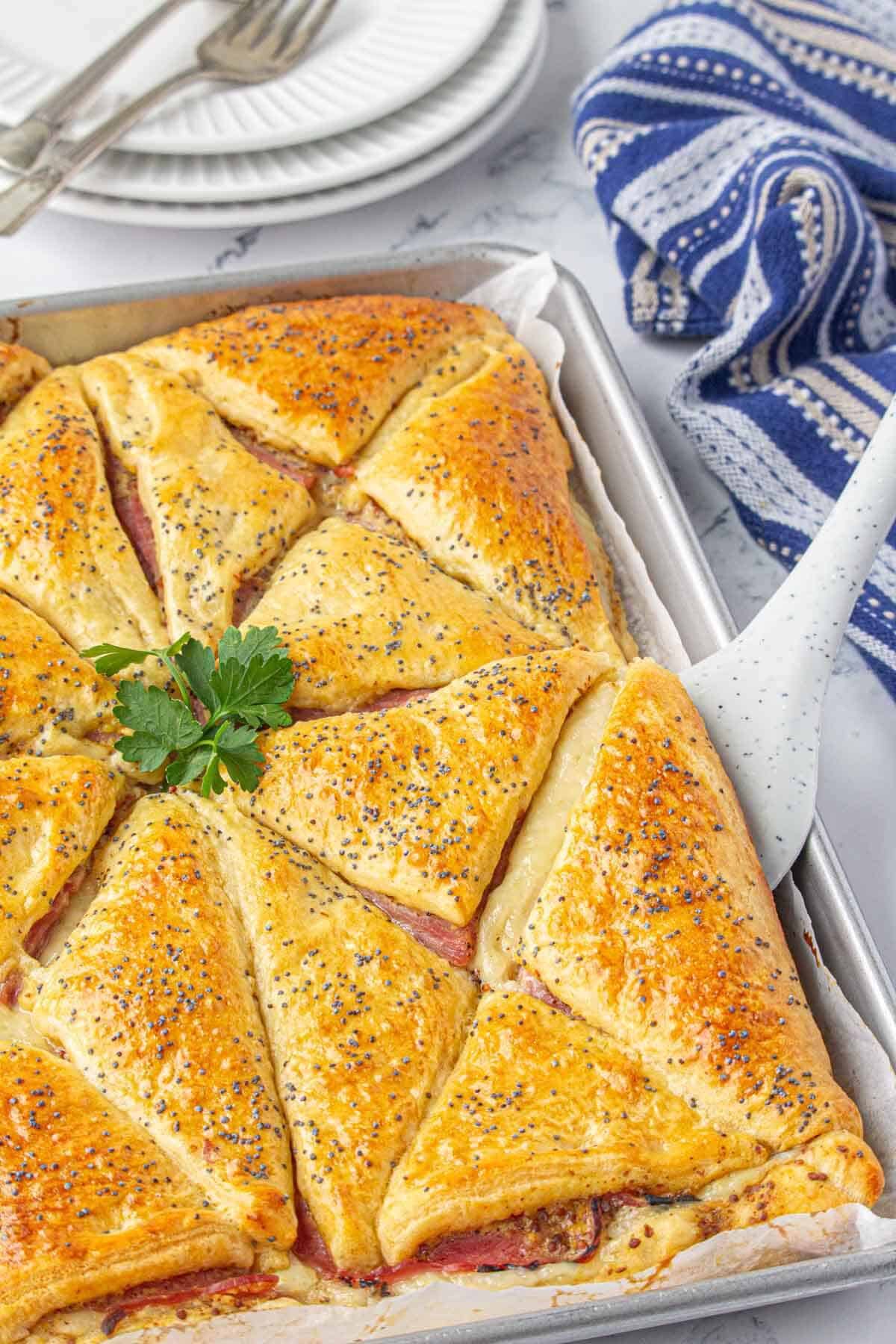 Golden brown baked ham and cheese sandwiches on a baking sheet. With a spatula serving up a sandwich.