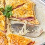 Sliced golden brown baked sandwiches on parchment paper. With a spatula on the side.