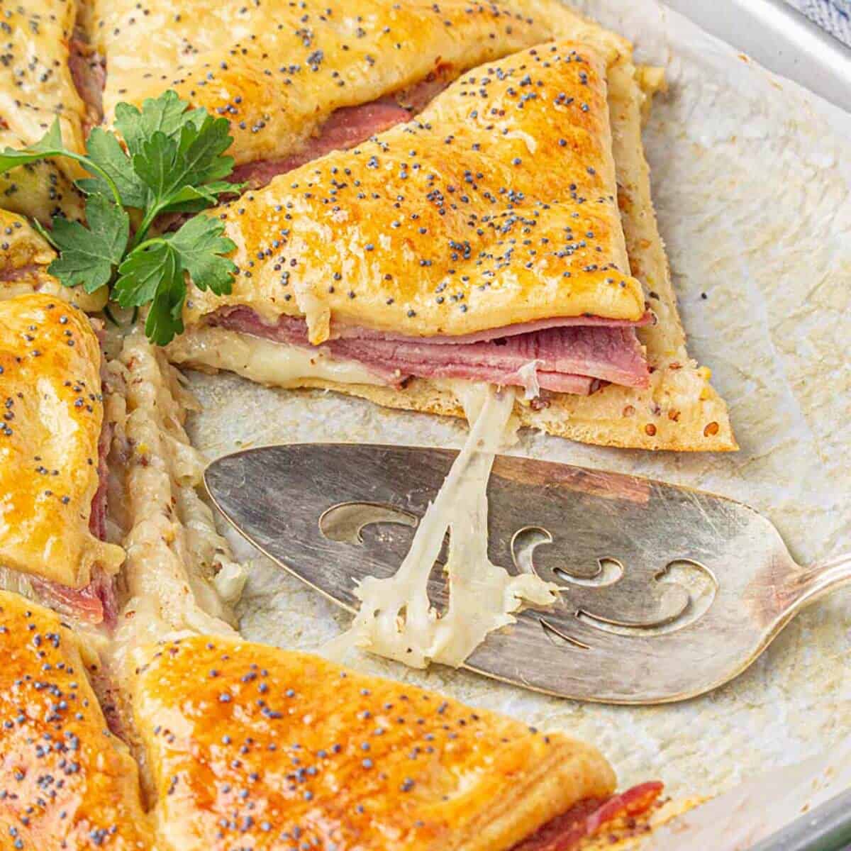 Sliced golden brown baked sandwiches on parchment paper. With a spatula on the side.