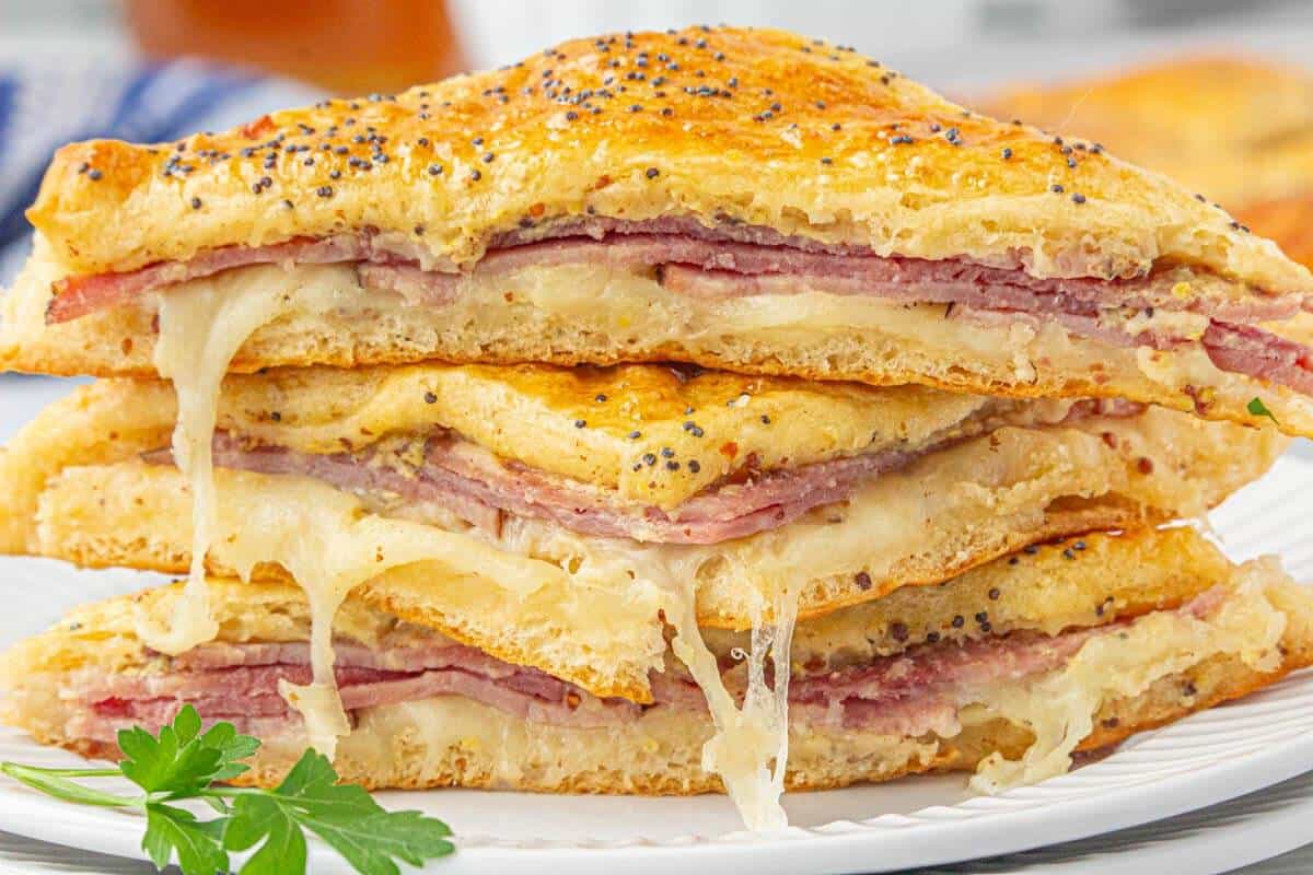 Sliced hot honey ham and cheese sandwiches stacked on a plate.